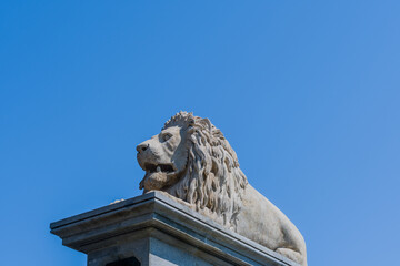 Stone lion statue atop a pedestal against a clear blue sky on a sunny day, in Budapest, Hungary