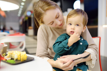Cute blonde little boy eating in a fast food courte cafe or restaurant with his young mother during...