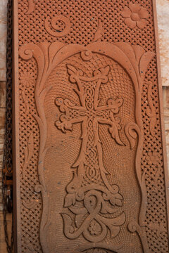 Vertical photo. Red brick slab with cross, flower and religious pattern in workshop against blue wall. Yerevan, Armenia. Process restores medieval Armenian cross stone called khachkar. Old grave. Job