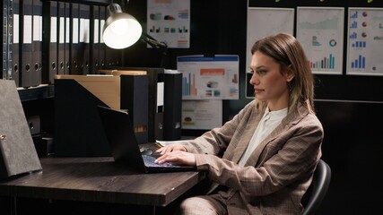 Confident female private detective investigator reviews clues in office, searching on laptop for evidence to solve crime. Profile portrait of focused caucasian policewoman using personal computer. - obrazy, fototapety, plakaty