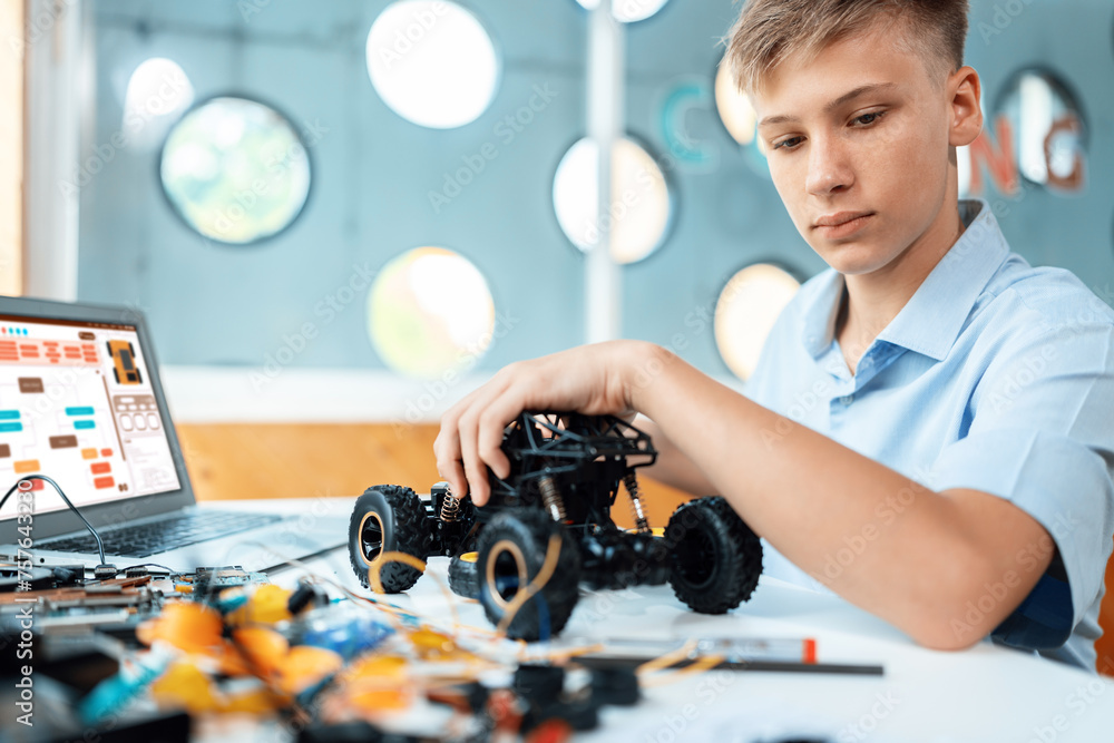 Poster schoolboy watching and considering parts of robotics car while learning technology in stem class. on