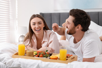 Obraz na płótnie Canvas Happy couple eating tasty breakfast on bed at home