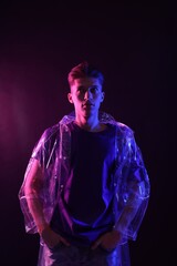 Young man wearing clear coat on dark background in neon lights