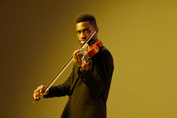 African American man in suit playing violin on yellow background, musical performance concept with elegant musician in formal attire