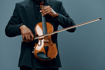 Elegant African American man in tuxedo playing the violin on gray background in a classical music performance