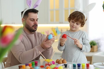 Easter celebration. Father with his little son painting eggs at table in kitchen