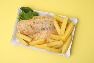 Delicious fish and chips with spinach and lettuce on yellow table, top view