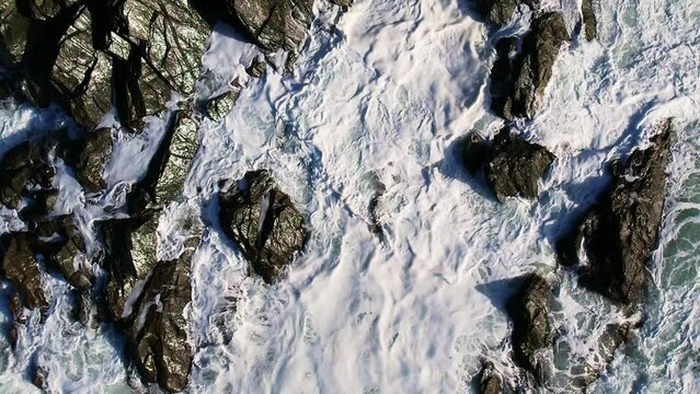 Slow Motion Ocean Waves and White Foam Crashing Over Cornish Rocks with an Aerial Top Down Shot.