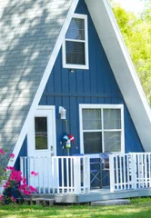 Keuken spatwand met foto Close up of cute adorable A frame triangle shaped house or home with deep blue color, grey shingle roof, white door, wood front porch railing, pink red azalea flower blooms. Nautical theme decor © Chase D’Animulls