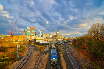A cityscape of Raleigh, North Carolina at sunset with a train on railroad tracks in the foreground. HDR.
