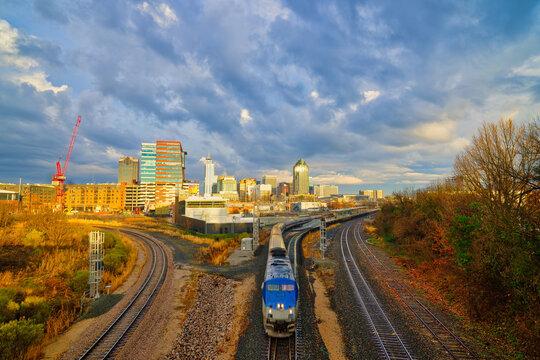 A cityscape of Raleigh, North Carolina at sunset with a train on railroad tracks in the foreground. HDR.
