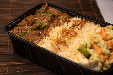 Beef Bhuna with pulao biryani rice with cucumber, dip sauce and lemon slice served in dish isolated on wooden table side view closeup of bangladeshi and indian spicy food