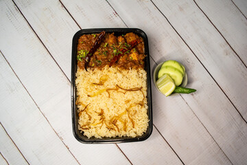 Achari chicken pulao biryani rice with cucumber and lemon slice served in dish isolated on wooden table top view of bangladeshi and indian spices lunch food