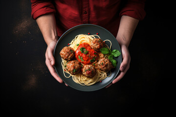 A man holding up spaghetti and meatballs on plate, top view, dark background, food photography - obrazy, fototapety, plakaty