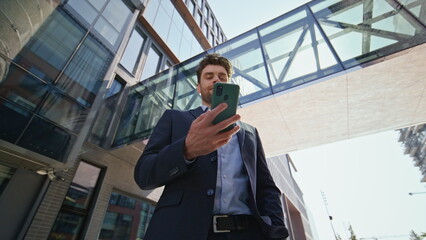 Confident entrepreneur looking cell phone screen on sunny street bottom view.