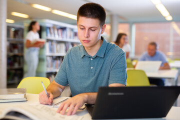Young male student studying with a laptop in the library. High quality photo