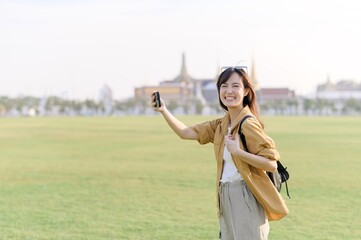 Traveler asian woman in her 30s take a livestream on smartphone while explores Wat Phra Kaew emerald Buddha. Share the wonders of Thai heritage through her journey.