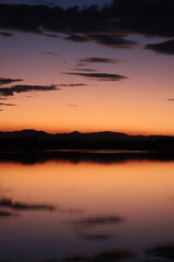 Colourful sunset over a flat lake with mountains in the background and clouds reflecting in water