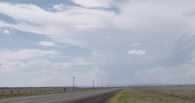 Wide shot of empty highway, clouds rolling overhead and a passing train in the distance
