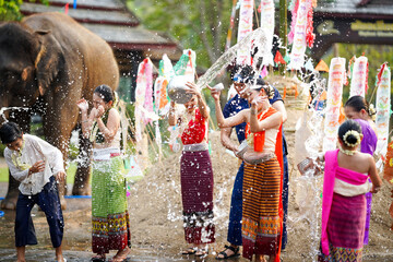 Group of Thai women and children ware Thai traditional dress play to splashing water on the Thai New Year's Day or Songkran festival in a fun way on elephant and pile of sand background. - obrazy, fototapety, plakaty