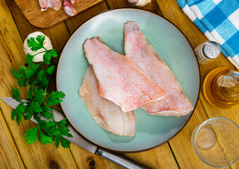 Three pieces of raw sea bass fillet on a plate while cooking in a home kitchen with a sprig of...