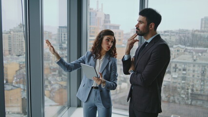 Colleagues sharing ideas standing window looking on city view. Smart coworkers 