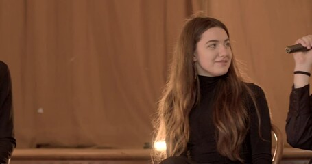 A school assembly where students and teachers deliver public speeches, congratulate, and applause rings out. The atmosphere is warm and cozy. A young Asian guy is speaking into a microphone, indoors.