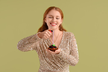 Beautiful young happy woman lighting candle on birthday cupcake against green background