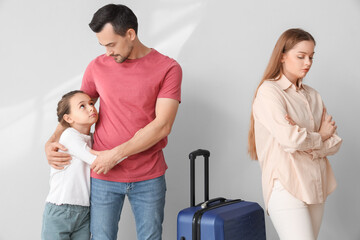 Sad little girl hugging her father before leaving on light background. Divorce concept
