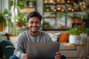 Smiling young man with laptop sitting comfortably at home surrounded by plants and warm lights, concept of remote work and cozy living