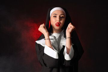 Naughty nun with handcuffs on dark background