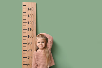 Cute little girl measuring height on green background