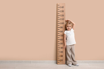 Cute little girl measuring height near beige wall