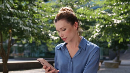 Fototapeta premium Business lady looking smartphone screen relaxing in sunny town park close up. 