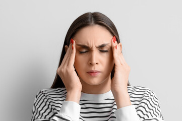 Young woman suffering from headache on light background, closeup