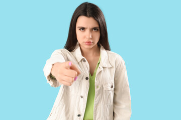 Young woman pointing at viewer on blue background. Accusation concept