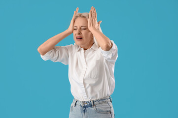 Mature woman suffering from headache on blue background