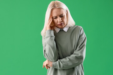 Mature woman suffering from headache on green background