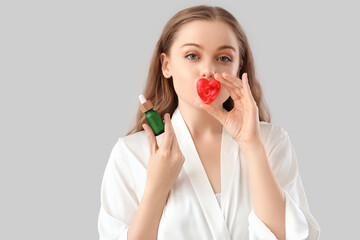 Beautiful young woman with heart-shaped soap and serum on light background, closeup