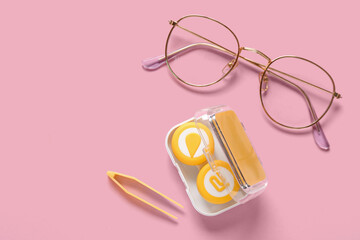 Stylish eyeglasses with tweezers and container for contact lenses on pink background