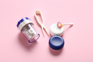 Containers with tweezers, holder and contact lens on pink background