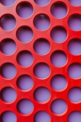 Detailed view of a bright red surface with small holes punched through, creating a pattern and texture