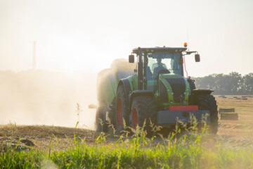 Combine harvester pressing straw from field into bales driving field on sunny summer evening. Field...