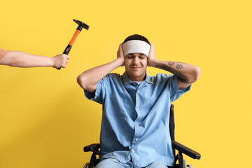 Young man with brain concussion in wheelchair and hammer on yellow background