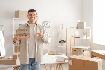 Male online store seller pointing at OPEN sign in warehouse