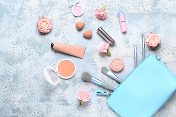 Cosmetic bag with makeup products and roses on blue grunge background