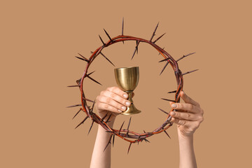 Female hands with crown of thorns and cup on color background, closeup. Good Friday concept