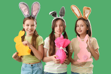 Cute little girls with Easter bunny ears, gift and decor on green background
