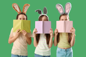 Cute little girl with Easter bunny ears and books on green background