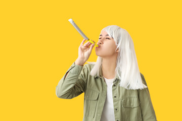 Beautiful young woman in funny disguise with party whistle on yellow background. April Fools Day...